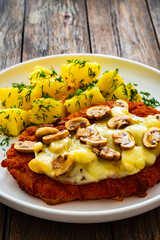 Crispy breaded seared pork chop with fried white mushrooms, cheese and boiled potatoes on wooden table
- 765590483