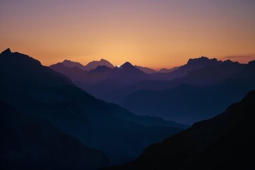 Obraz premium The sun dips below the mountains on the horizon, casting a warm glow over the rugged peaks in the distance
