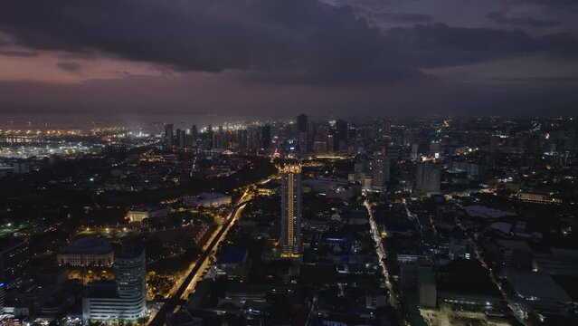 Beautiful evening aerial panoramic view of metropolis. Illuminated streets and buildings in large city. Harbor on sea coast in distance. Manila, Philippines