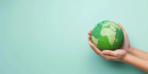 Foto op Aluminium A pair of hands holding a green earth globe against a light blue background, an image fitting for concepts related to global care or environmental education. © Ярослава Малашкевич