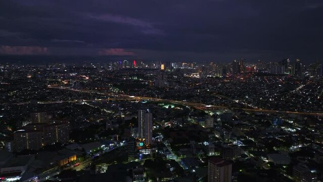 Aerial panoramic view of metropolis. Fly above buildings and streets in urban boroughs. Vehicles on busy thoroughfare and modern downtown high rises in distance. Manila, Philippines