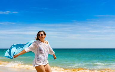 Beautiful woman walking on sunny beach holding shawl
- 765605250