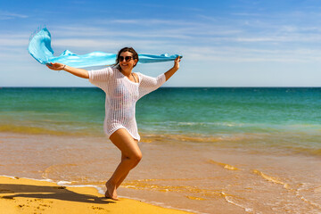 Beautiful woman walking on sunny beach holding shawl
- 765605405