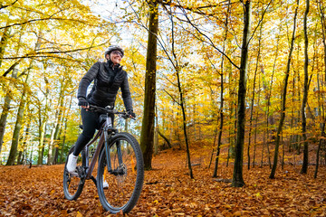 Woman riding bicycle in city forest in autumn scenery
