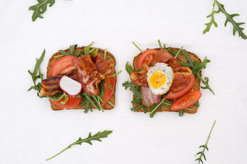 Two sandwiches with aragula, fried ham, tomatoes, fried egg on white background, top view.