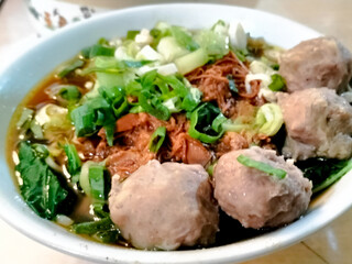 A bowl of traditional noodle called Mie Ayam Bakso taken from top angle. Top angle of Mie Ayam Bakso on a white bowl with meatball.