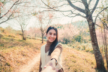 Young asian woman holding hands with her boyfriend enjoying in wild himalayan cherry blooming in springtime