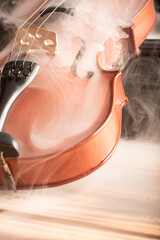 Violin with smoke, beautiful violin covered with a thin smoke screen on rustic wood and black background, selective focus.