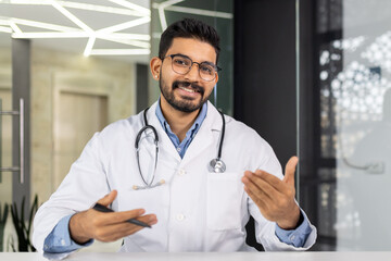 A doctor is smiling and holding a clipboard. He is wearing a white lab coat and glasses. The clipboard has a pen on it