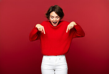 Excited, attractive woman pointing down with her forefingers, isolated on a red background