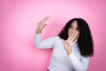 African american woman wearing casual sweater over pink background scared with her arms up like...