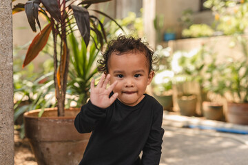 Adorable Asian toddler in casual attire waving hello in a garden setting © Mdv Edwards