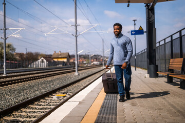Happy man with suitcase walking on railway station.