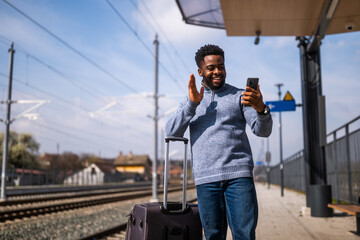 Happy man  with a suitcase taking selfie and waving on a railway  station.