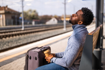 Tired man with a coffee sleeping on a bench at the railway station.	