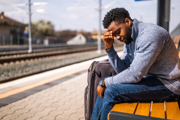 Worried man with a suitcase sitting on a bench at the railway station. - 765635051