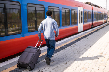 Man running to a leaving train along railway station with suitcase.