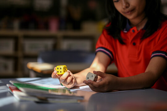 girl student at her desk working on maths problems using dice