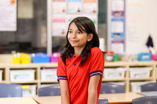 Female school student in a red polo shirt thoughtfully standing in classroom