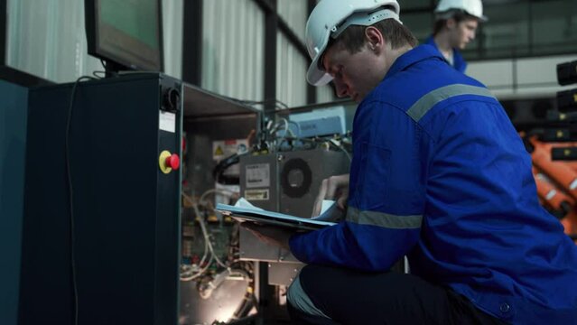 Factory workshop: professional male engineer Male machine operator uses an industrial digital tablet computer to operate and program a robot arm for the production line. High tech facilities with mach
