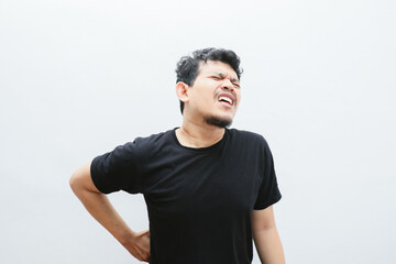 an asian man holds his back and looks in pain