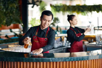 Smiling bartender wiping bar counter in the beginning of shift