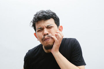 an asian man holds his cheek and looks in pain