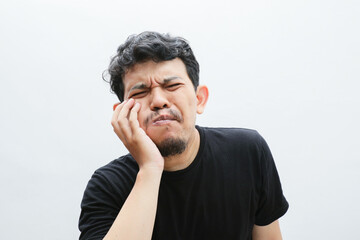 an asian man holds his cheek and looks in pain