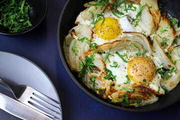 Uova fritte fatte in casa e finocchio con erbe in una padella di ferro su sfondo grigio. Cibo sano e vegetariano. Vista dall'alto. - 765649047