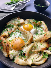 Uova fritte fatte in casa e finocchio con erbe in una padella di ferro su sfondo grigio. Cibo sano e vegetariano. Vista dall'alto. - 765649095