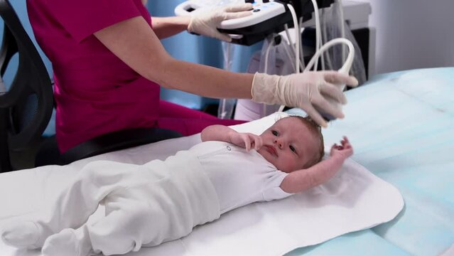 A female doctor conducts an ultrasound examination of the head and brain of a newborn baby using modern medical equipment in a clinic. Pediatrics and control of the development of the child's body.