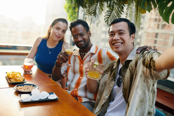 Smiling Vietnamese man taking selfie with best friends in bar