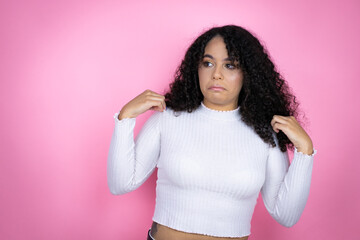 African american woman wearing casual sweater over pink background holding her t-shirt with a...