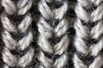 Close-up of hand-knitted wool fabric with voluminous braids. Natural black and white wool textile background. Warm woolen cozy clothes. Flat lay, macro, top view, mockup