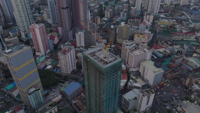 Fly around crane on top of construction of modern building. High angle view of town development. Manila, Philippines