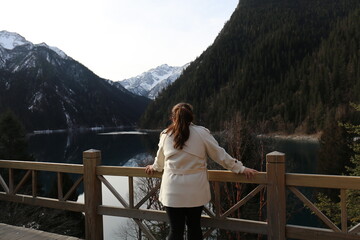 Young woman standing on a wooden bridge and looking at the mountains.