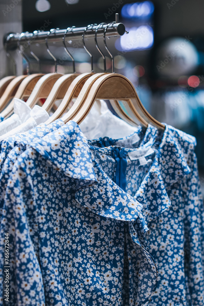 Wall mural Summer fashion collection. Blue women's dresses with floral pattern hanging on a hangers in a row.