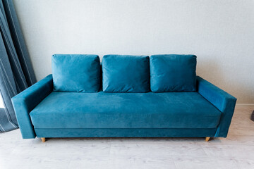 Electric blue studio couch with pillows in a living room next to a window