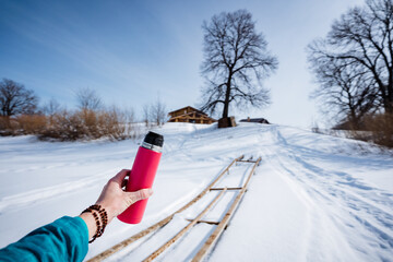 Person holds pink bottle in snowy landscape, surrounded by trees