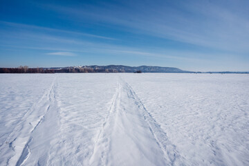 Fototapeta na wymiar Tire tracks cut through snowy field under cold winter sky