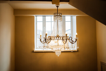 An amber chandelier hangs from the ceiling in front of a window