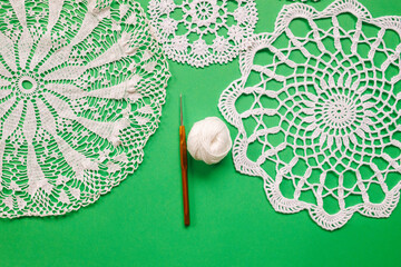 crocheted napkins and crochet hook on a green background close-up. Handicrafts as a way of...