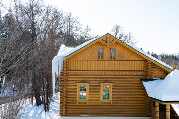 Snowcovered log cabin with icicles on the roof, overlooking a forested slope