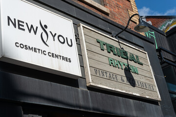 Fototapeta premium exterior building facade and signs of New You Cosmetic Centres and Tribal Rhythm Vintage Accessories at 248 Queen Street West in Toronto, Canada