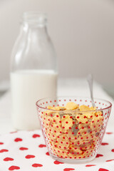 Tasty corn flakes with granola in bowl with bottle of milk. Rustic background with beautiful napkin with heart print. Healthy crispy breakfast snack. The concept of a healthy lifestyle. - 765692691