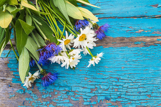 Mother's day greeting card template; Bunch of wild flowers: white daisies and blue cornflowers on a old blue paint wooden background; copy space