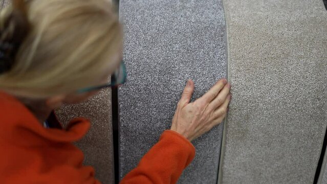 Attractive mature woman shopping for carpet looking through samples for home redecorating project, in a hardware store.