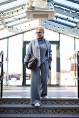 Attractive and stylish mature woman in grey pant suit with jacket and turtleneck, accessorized with...