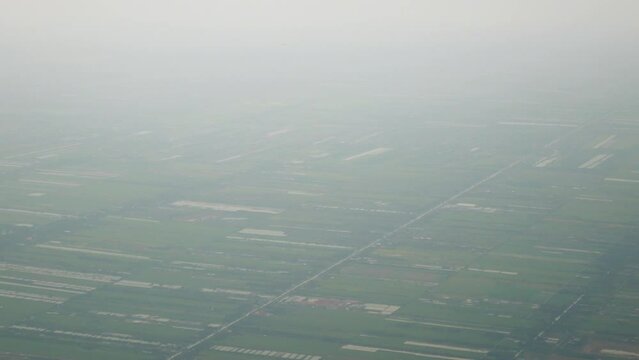 aerial view from flying aircraft with view of the green farm field area with thin layer of smog or fog smoke pm2.5 pollution in the sky