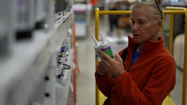 Woman looking at tubes of caulk in a hardware store, comparing products. Concept of home remodeling shopping experience.